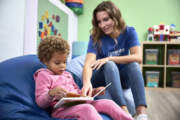 A behavior technician is sitting down and reading with a child.